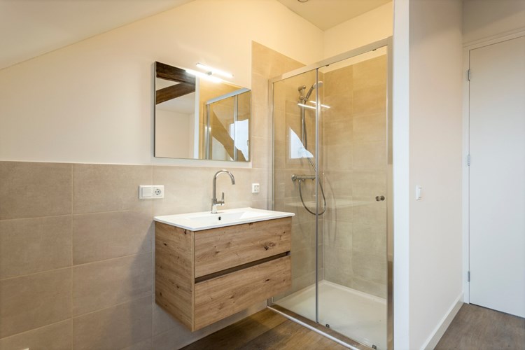 Deze ruimte is voorzien van een inloopdouche met een glazen schuifdeur en een thermostaatkraan, een badmeubel met een wastafel en een spiegel en mechanische ventilatie.
