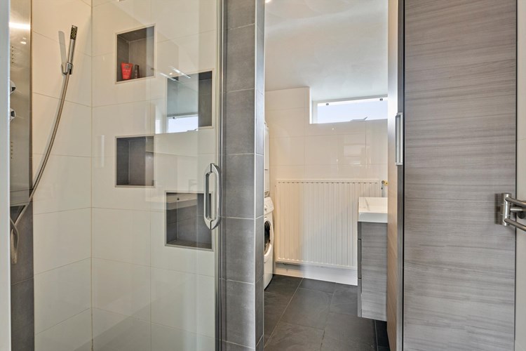 Moderne badkamer (2015) met een antraciet tegelvloer, volledig licht betegelde wanden en een stucwerk plafond. Voorzien van een royale douchecabine met een 'stort' douche, een thermostaatkraan en een glazen deur. Praktische opbergnisjes.