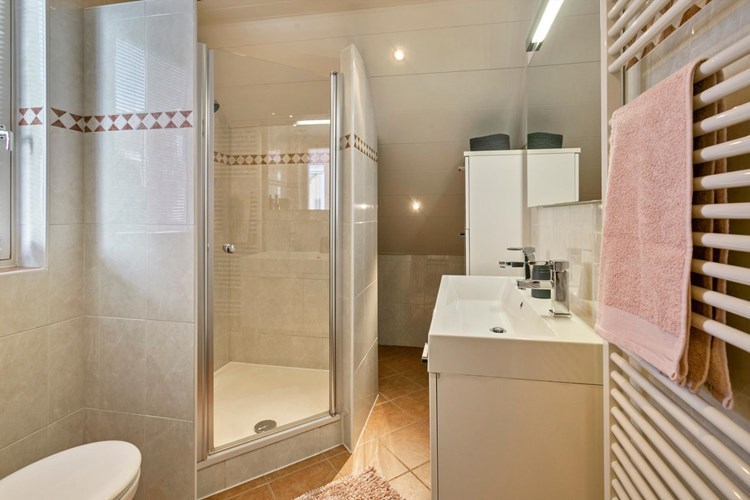 De volledig, licht betegelde badkamer is voorzien van MDF plafond met inbouwspots. Met een designradiator en een badmeubel met een badmeubel met wastafel met dubbele kraan en en een grote spiegel. 