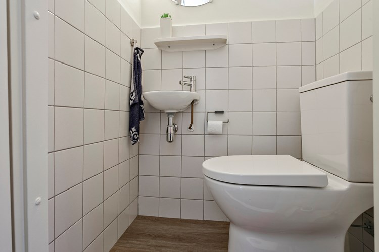 Toilet met een PVC vloer, gedeeltelijk betegelde wanden en een spuitwerk plafond. Met een duoblok en een fonteintje. Natuurlijke ventilatie middels een raampje. 