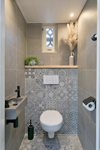 Modern toilet (2021) met een tegelvloer, volledig betegelde wanden en een kunststof panelen plafond met inbouwspots. Met een wandcloset, een fonteintje en natuurlijke ventilatie middels een raampje. 