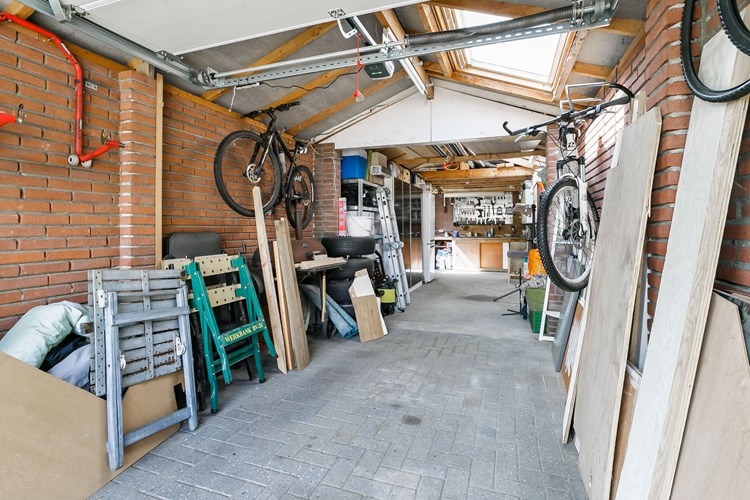 De garage is deels voorzien van een betonvloer en deels met klinkers, gedeeltelijk met spouwmuren en een zadeldak met pannen gedekt. Daglicht via een tweetal dakramen. 