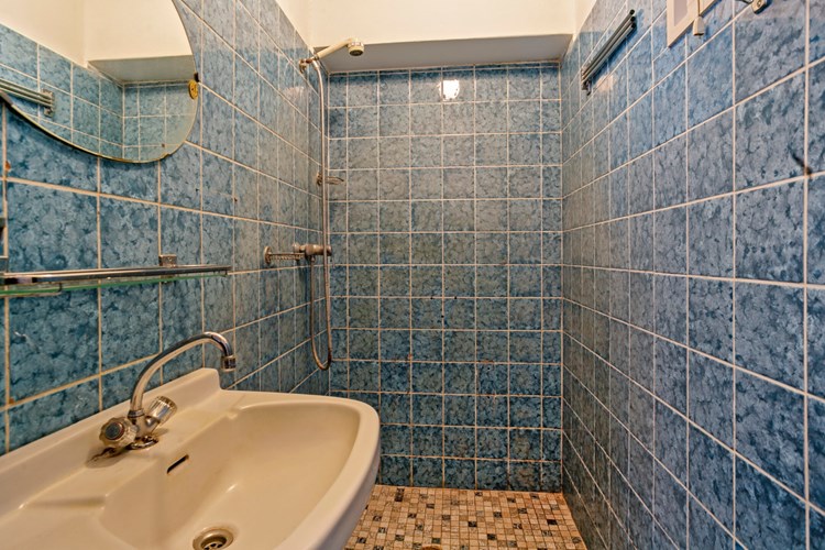 Een eenvoudige doucheruimte met een inloopdouche en een wastafel. Voorzien van gedeeltelijk betegelde wanden en een stucwerk plafond.