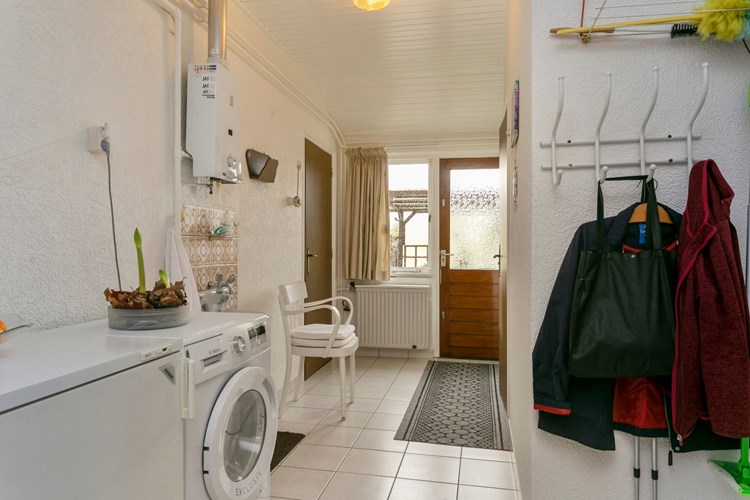 Bijkeuken met een licht tegelvloer, granol wanden en een licht schroten plafond. Hier bevindt zich de aansluiting voor de wasapparatuur en de Vaillant badgeiser t.b.v. de douche en keuken. 