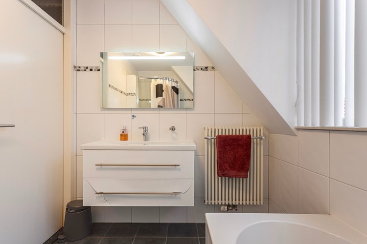 De badkamer is voorzien van een antraciet tegelvloer, volledig licht betegelde wanden en een spuitwerk plafond. Met een badmeubel met vaste wastafel en een spiegel met verlichting. 