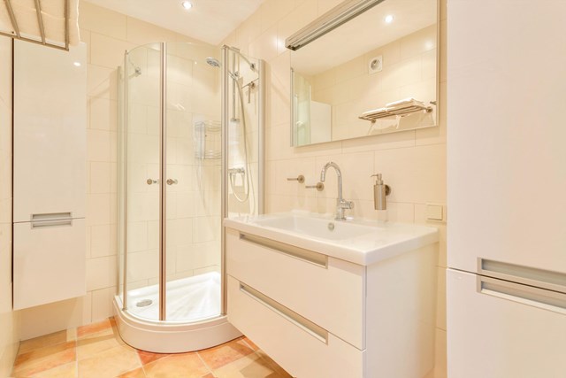 De badkamer heeft een douchecabine en badmeubel met wastafel en extra kastruimte. De lichte kleurstelling zorgt voor een frisse en aangename uitstraling.