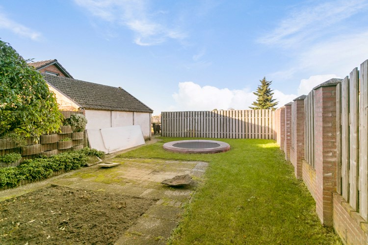 De tuin is volledig omheind, met aan de rechterzijde van de woning een gazon, grenzend aan de aangebouwde hobbykamer. 