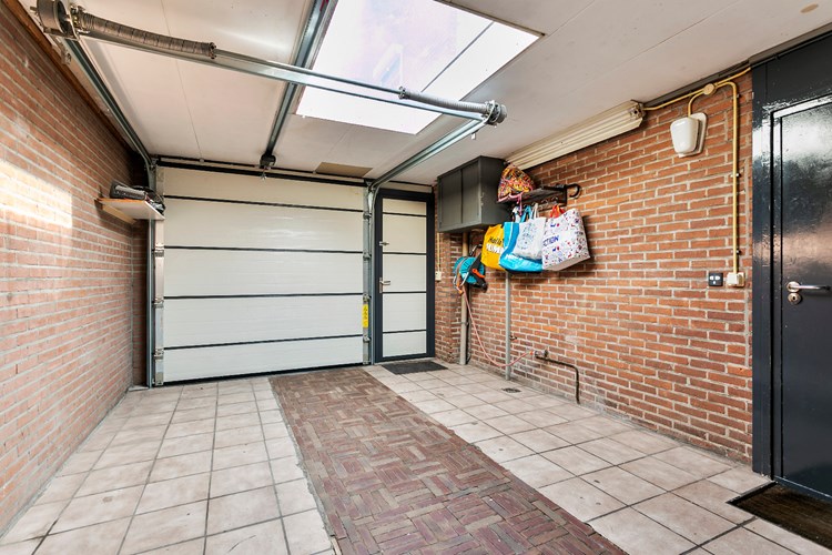 Vanuit de oprit toegang tot de royale garage middels een automatische, geïsoleerde sectionaaldeur met aparte loopdeur. De royale garage is ook bereikbaar vanuit de bijkeuken en de achtertuin.
