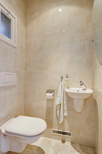 Modern toilet met een lichte tegelvloer, volledig licht betegelde wanden en een aluminium panelen plafond met inbouwspots. Met een wandcloset en een fonteintje. Natuurlijke ventilatie middels een raampje. 