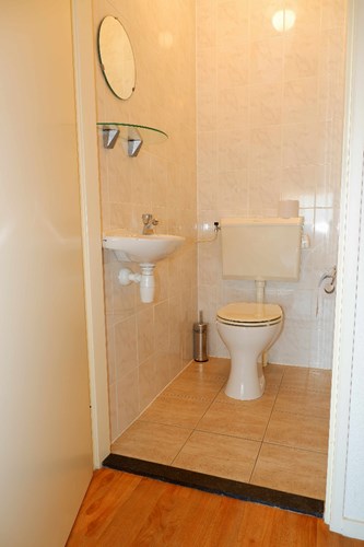 Toilet met een lichte tegelvloer, volledig licht betegelde wanden en een spuitwerk plafond. Voorzien van een duoblok, een fonteintje en mechanische ventilatie. 
