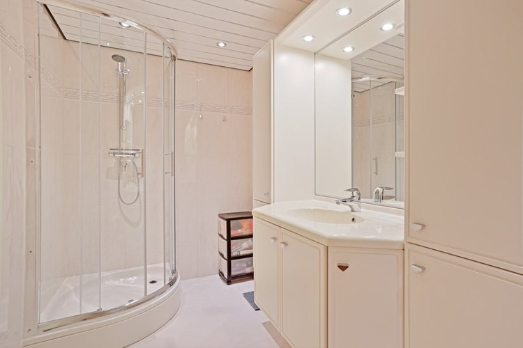 Ruime badkamer met  een lichte tegelvloer, volledig licht betegelde wanden en een aluminium plafond met inbouwspots. Met een badmeubel met vaste wastafel met inbouwspots en een grote spiegel, een douchecabine met glazen schuifdeuren en een thermostaatkraan.