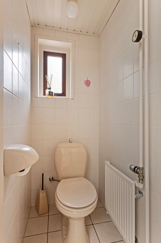 Het toilet is voorzien van een lichte tegelvloer, volledig licht betegelde wanden en een schroten plafond. Met een duoblok, een radiator en een raampje. 