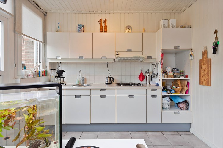 Keuken met een lichte tegelvloer, licht schroten wanden en een licht schroten plafond. Met een lichte keukeninrichting voorzien van een RVS gaskookplaat, een afzuigkap en een ronde RVS spoelbak. 