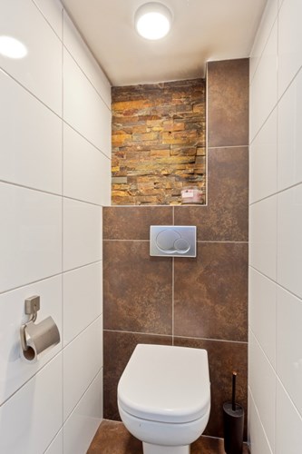 Modern toilet met een tegelvloer, volledig betegelde wanden en een stucwerk plafond. Voorzien van een wandcloset met een opzetplateau. 