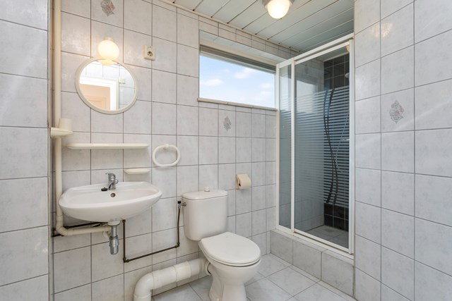 De badkamer is geheel betegeld en voorzien van wastafel, toilet en douchecabine