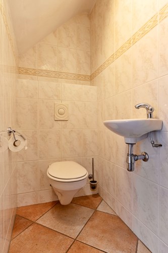 Het toilet is voorzien van een diagonaal gelegde tegelvloer en volledig betegelde wanden. Met een wandcloset met opzetplateau, een fonteintje en mechanische ventilatie. 
