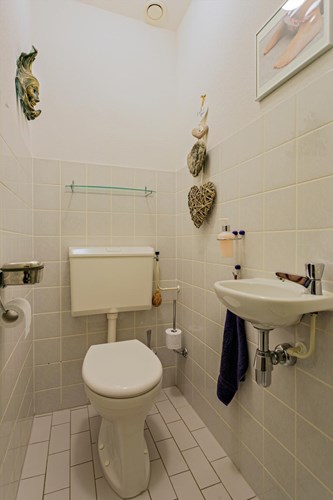 Toilet met een lichte tegelvloer, gedeeltelijk betegelde wanden en een spuitwerk plafond. Met een fonteintje en mechanische ventilatie. 