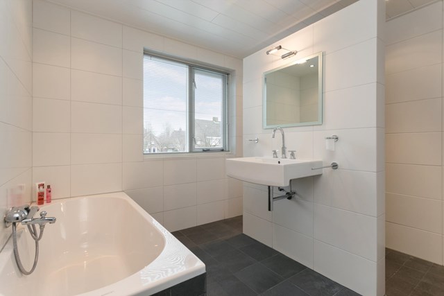 De prachtige, moderne badkamer is zeer functioneel ingericht.
Achter de vrijstaande wand met wastafel vindt u......