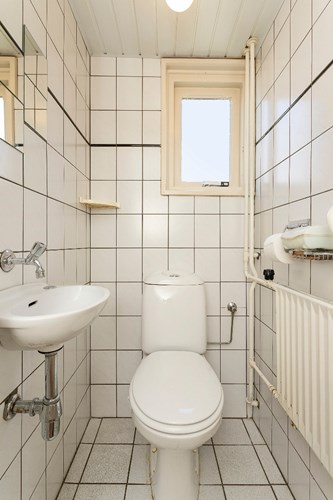 Volledig licht betegeld toilet met een kunststof schroten plafond. Een duoblok en een fonteintje. Daglicht en ventilatie via een hardhouten raamkozijn met dubbele beglazing. 