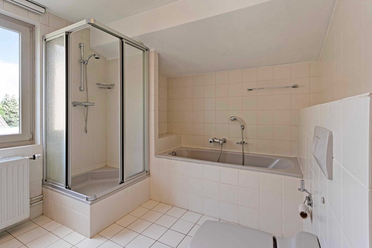 De volledig betegelde badkamer is voorzien van een kunststof ligbad met opzetplateau, een separate douchecabine met een thermostaatkraan en een wandcloset met opzetplateau.