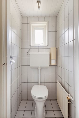Een volledig betegeld toilet met een kunststof schroten plafond. Met een duoblok, een radiator en een raampje. 