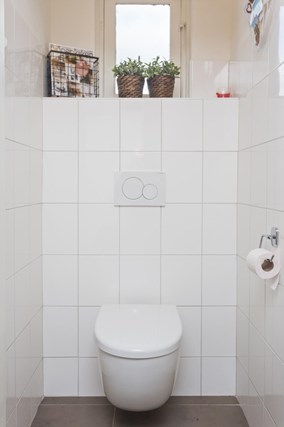 De toiletruimte met zwevend toilet en neutrale witte betegeling op de wanden.