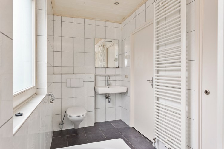 Op de overloop (bij de trap), badkamer met een tegelvloer, volledig licht betegelde wanden en een MDF plafond met inbouwspots. Met een wandcloset, een wastafel met spiegel en een muurkast. 