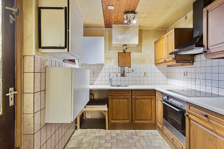De keuken is gelegen in de aanbouw, met een tegelvloer, gedeeltelijk betegelde wanden en een schroten plafond. Keukeninrichting in een hoekopstelling voorzien van een ronde RVS spoelbak, een keramische kookplaat, een elektrische oven en een afzuigkap. 