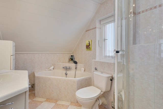De badkamer is geheel betegeld en voorzien van hoekbad, douche, badmeubel en 2e toilet.