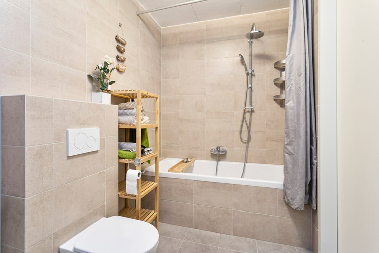 Badkamer met een tegelvloer, volledig betegelde wanden en een gipsplaten spuitwerk plafond. Voorzien van een kunststof ligbad met douche mogelijkheid en een wandcloset met opzetplateau. 