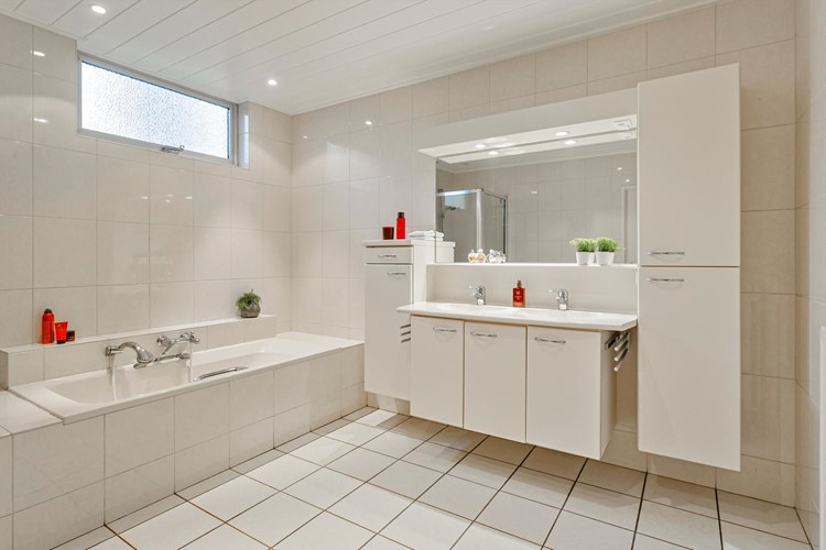 De badkamer is volledig betegeld en voorzien van een MDF panelen plafond met inbouwspots. Met een groot badkamermeubel met dubbele wastafel, een grote spiegel en veel kastruimte. Een kunststof ligbad met een opzetplateau. 