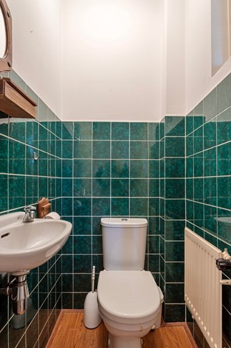 Toilet met een parketvloer, gedeeltelijk betegelde wanden en een stucwerk plafond. Met een duoblok, een fonteintje en een raampje. 