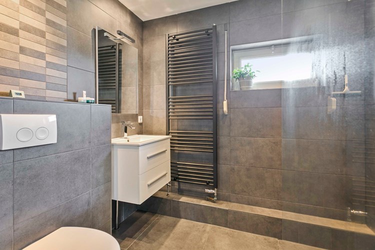 Een moderne, luxe badkamer met een tegelvloer, volledig betegelde wanden en een stucwerk plafond met inbouwspots. 