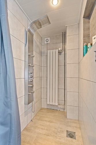 Een separate, volledig betegelde doucheruimte met een kunststof panelenplafond met inbouwspots. Voorzien van een inloopdouche met een regendouche en zijspoeiers. Mechanische ventilatie aanwezig.