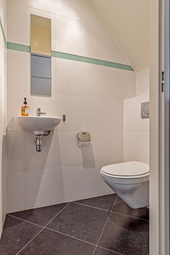 Modern toilet met een antraciet tegelvloer, volledig licht betegelde wanden en een stucwerk plafond met inbouwspots. Voorzien van een wandcloset met een opzetplateau, een fonteintje en mechanische afzuiging. 