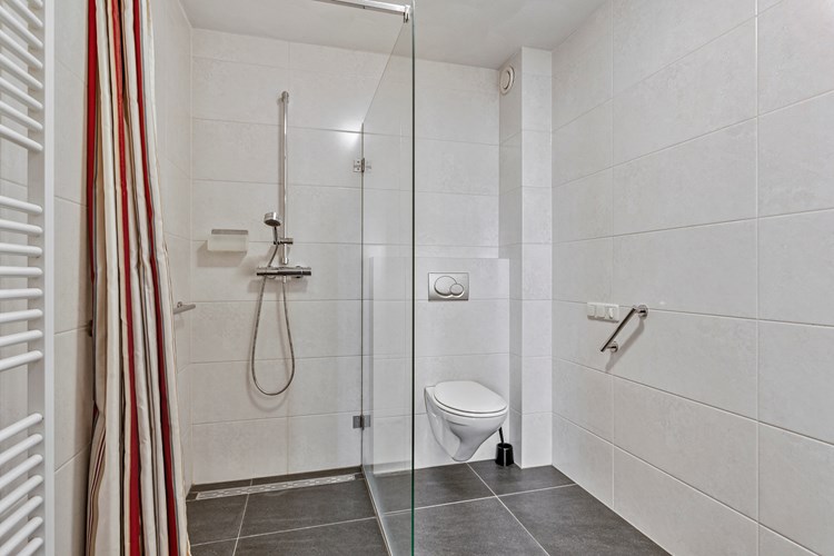 Moderne badkamer met een antraciet tegelvloer met vloerverwarming, volledig betegelde wanden en een stucwerk plafond. Met een inloopdouche met een thermostaatkraan en een wandcloset met opzetplateau. 