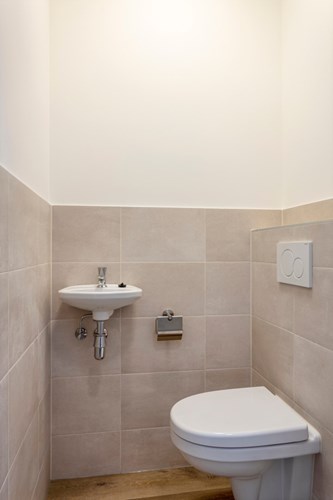 Een modern, gedeeltelijk betegeld toilet met een wandcloset met een opzetplateau, een fonteintje en mechanische ventilatie.