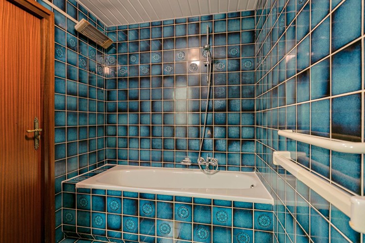 Een volledig betegelde badkamer met een kunststof schrotenplafond. Voorzien van een stalen ligbad.