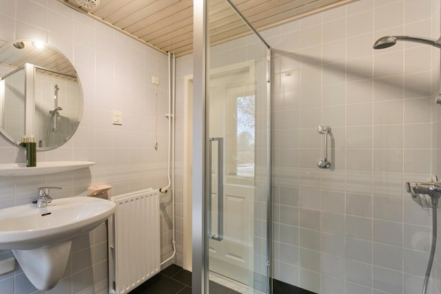 De praktisch ingedeelde badkamer beschikt over een ligbad, separate douche met glazen afscheiding, wastafel en tweede toilet.