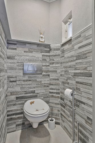 Modern toilet met een lichte tegelvloer, grotendeels betegelde wanden en een panelen plafond met inbouwspots. Met een wandcloset en een raampje. 