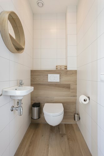 Modern toilet met een 'houtlook' tegelvloer, volledig licht betegelde wanden en een stucwerk plafond. Met een wandcloset met opzetplateau en een fonteintje. 