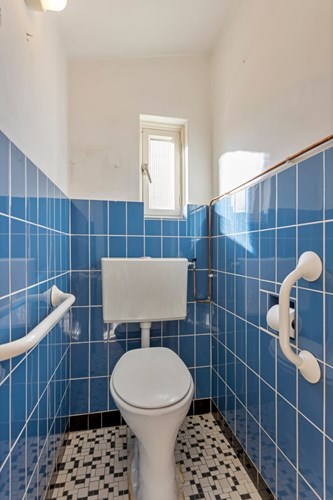 Het toilet is gedeeltelijk betegeld en heeft natuurlijke ventilatie via een houten raampje.