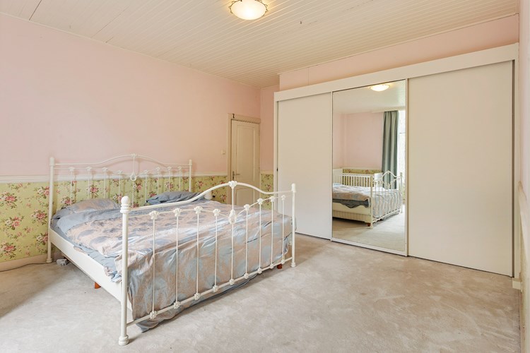 Op niveau 2 ligt een ruime slaapkamer met vloerbedekking, lambrisering wanden en een licht schroten plafond. Met een vaste schuifwand kast (3-deurs) met spiegel. De deur geeft toegang tot de grote bergruimte onder het lessenaarsdak.