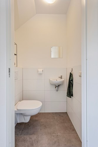 Modern gedeeltelijk betegeld toilet met een tegelvloer. Voorzien van een wandcloset en een fonteintje. 