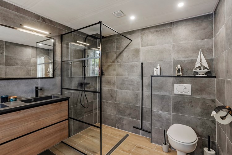 De badkamer is voorzien van een tegelvloer (houtlook), volledig betegelde wanden en een stucwerk plafond met inbouwspots en mechanische ventilatie.