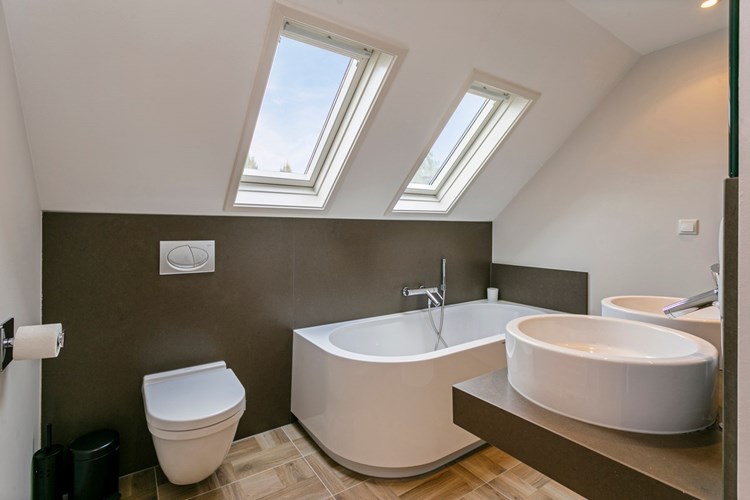 De moderne en luxe afgewerkte badkamer is voorzien van een 'houtlook' tegelvloer en gedeeltelijk betegelde en gestucte wanden. Met een wandcloset en een tweetal waskommen met een spiegel. 