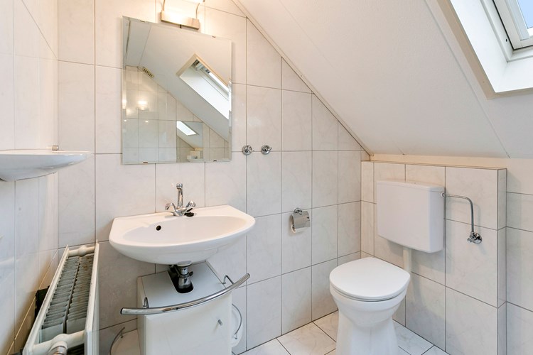 Badkamer met een lichte tegelvloer, volledig licht betegelde wanden en een spuitwerk plafond. Voorzien van een wastafel met spiegel en een 2e toilet. 