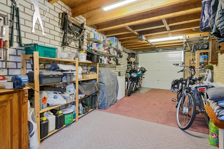 Garage met een betonvloer met vloerbedekking en een plat bitumen dak. Hier bevindt zich een extra groepenkast met o.a. krachtstroom, een radiator en een waterontharder. 