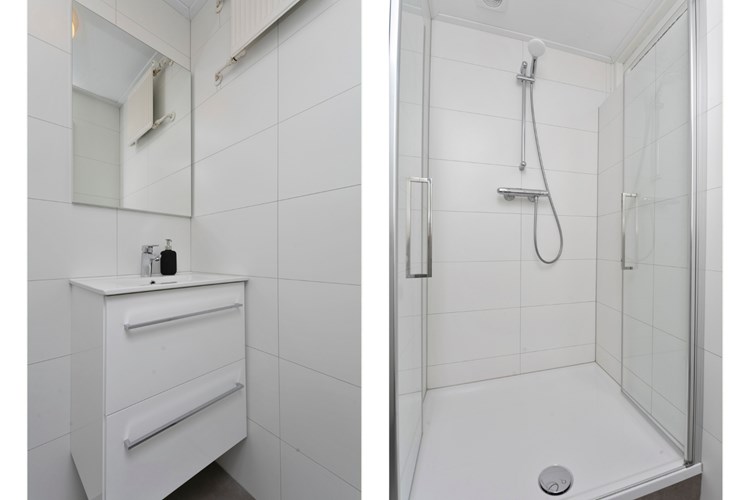 Een moderne badkamer met een antraciet tegelvloer en volledig licht betegelde wanden. Met een badmeubel met vaste wastafel, een spiegel en een douchecabine met glazen deuren en een thermostaatkraan.  