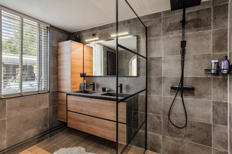 Deze moderne badkamer heeft een inloopdouche met een regendouche en een thermostaatkraan, een badmeubel met dubbele wastafel, grote spiegel en verlichting, een wandcloset met opzetplateau en een designradiator.